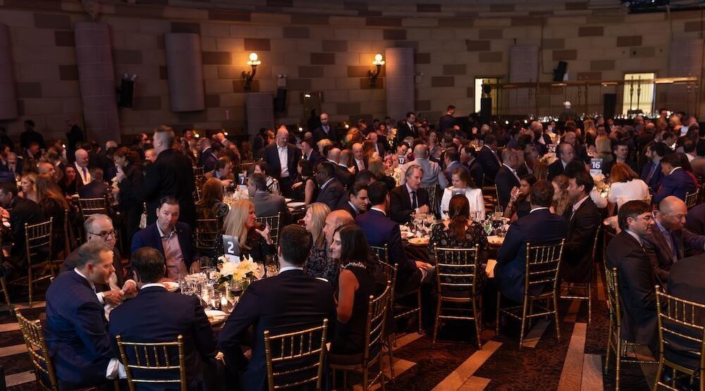 A ballroom with large roundtables filled with people having food at the awards event