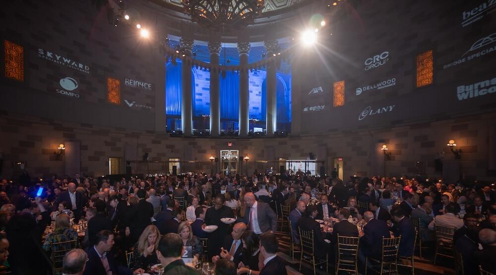 A ballroom with large roundtables filled with people having food at the awards event