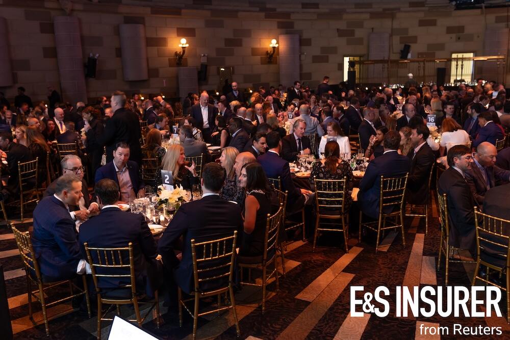 A ballroom with large roundtables filled with people having food at the awards event