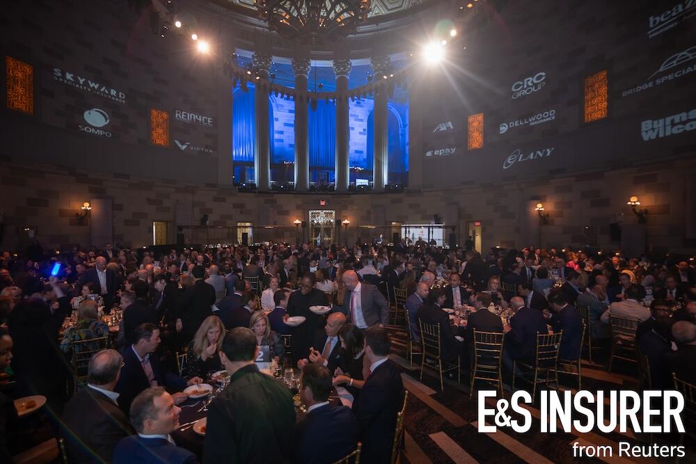 A ballroom with large roundtables filled with people having food at the awards event