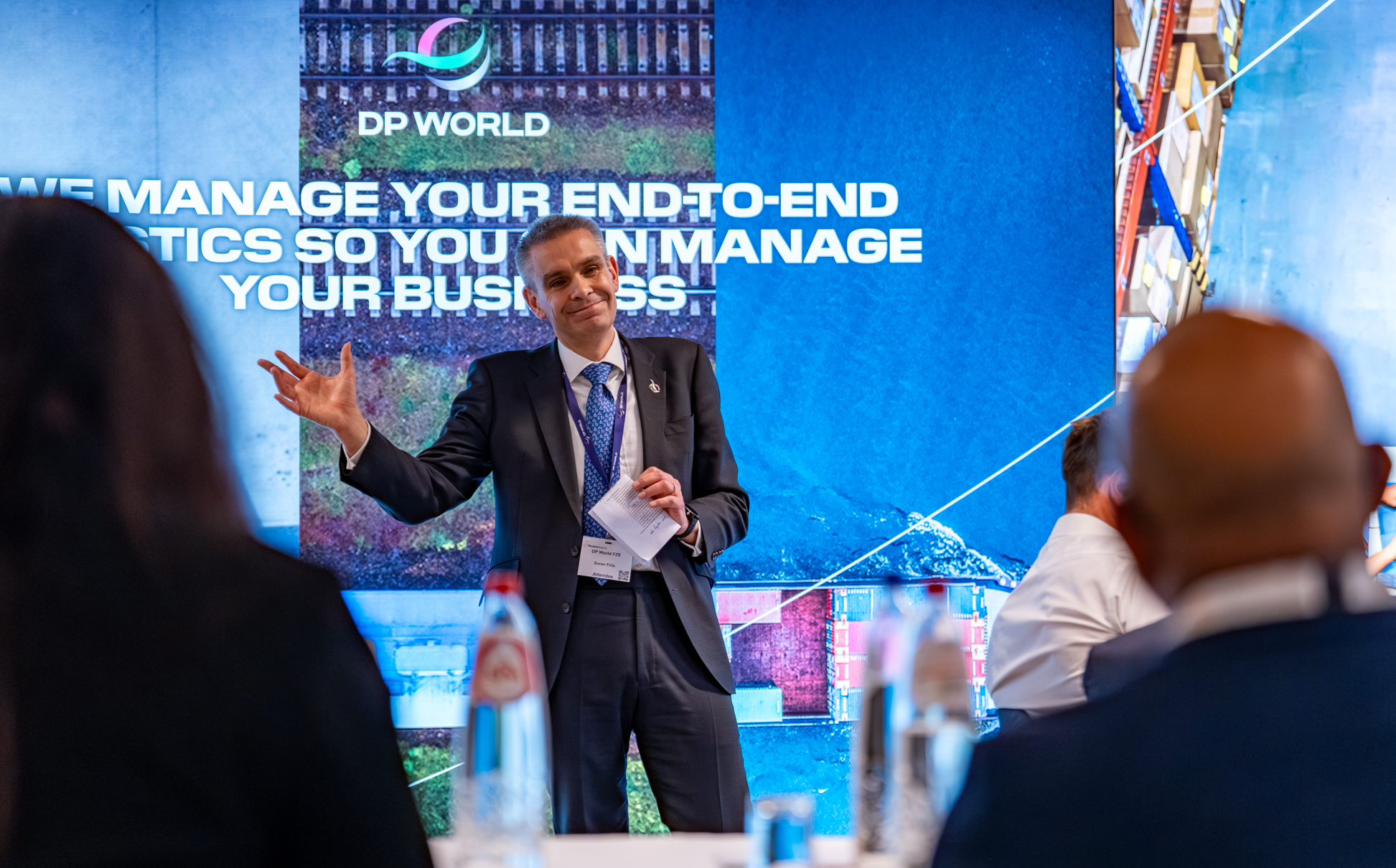 Man speaking to attendees in front of a DP World display.