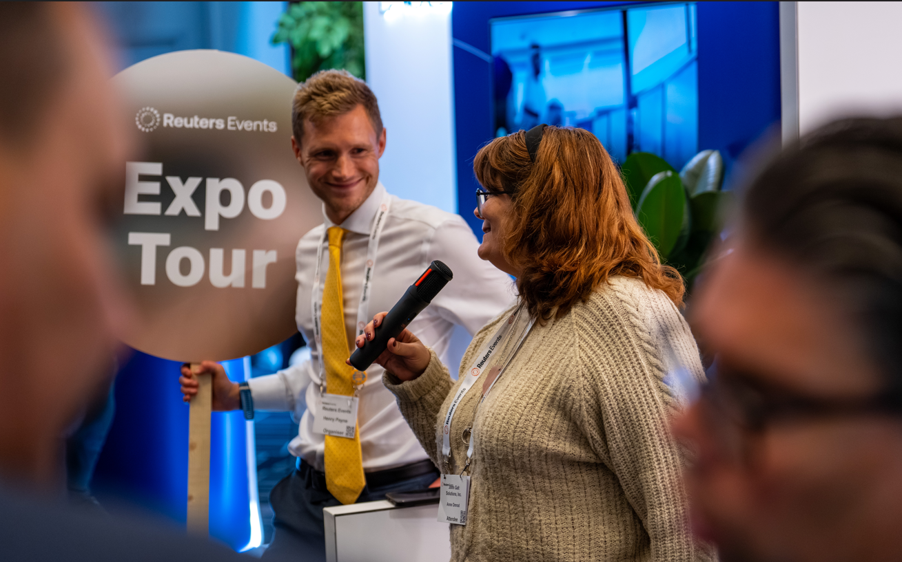 Attendee speaking into a microphone beside a Reuters Events Expo Tour sign.