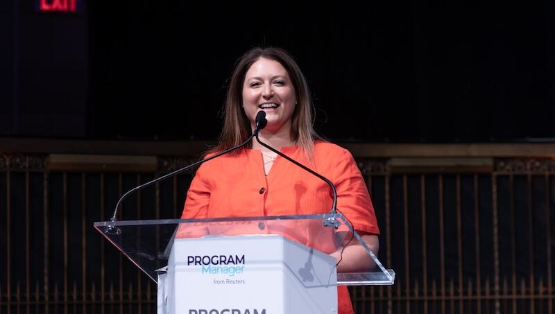 Presenter on stage at a podium smiling