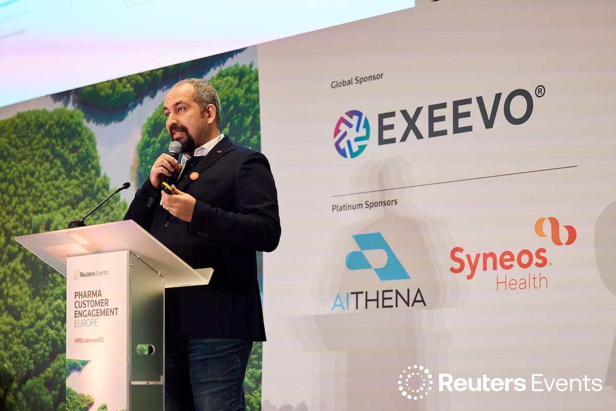 Person on stage at a Reuters Events conference giving a presentation holding a microphone up to their mouth. 
