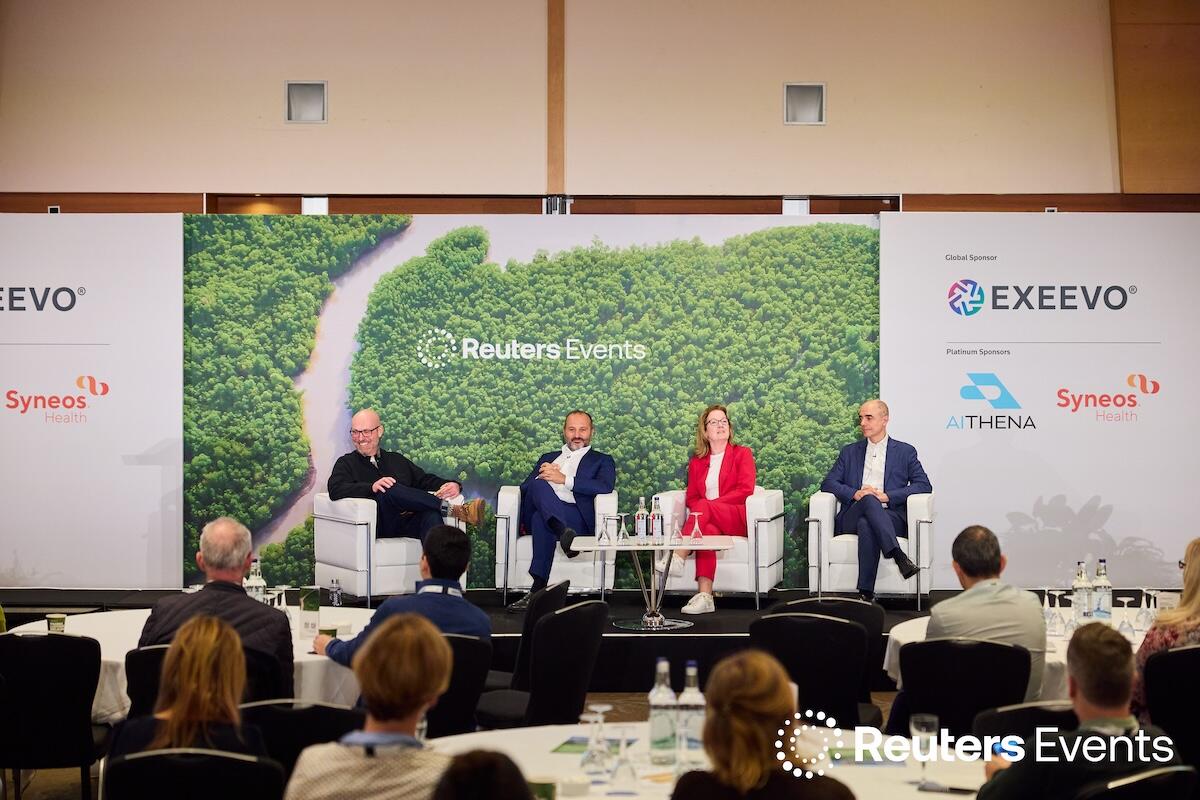 4 people on stage at a Reuters Events conference giving a panel presentation to a room full of people
