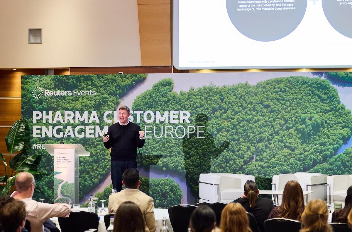 A speaker on stage at a Reuters Events conference giving a presentation. 