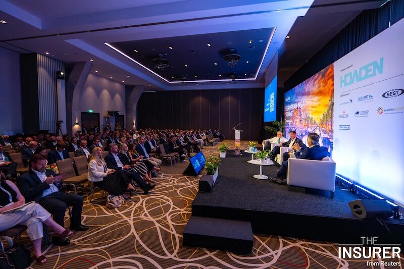 A photo of 3 presenters on stage at an event giving a presentation to a room full of people