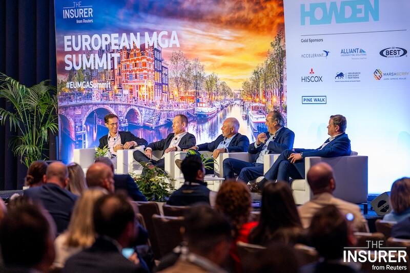 Five speakers sitting in white chairs on stage at the European MGA summit last year. 