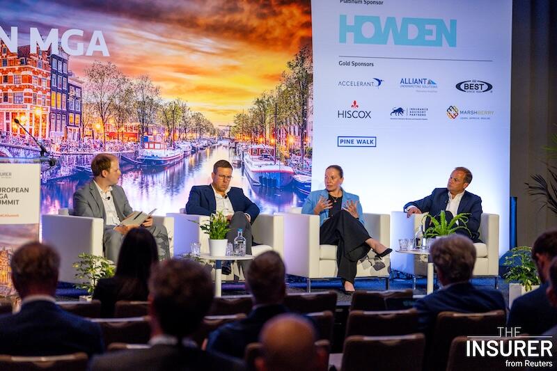 A close up shot of four speakers sitting in white chairs on stage at the European MGA summit last year. 