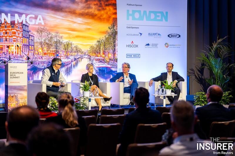 Four speakers sitting in white chairs on stage at the European MGA summit last year. 