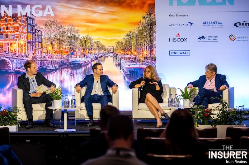 A close up shot of four speakers sitting in white chairs on stage at the European MGA summit last year. 