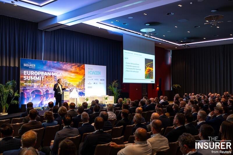 A photo of a presenter on stage at an event giving a presentation to a room full of people