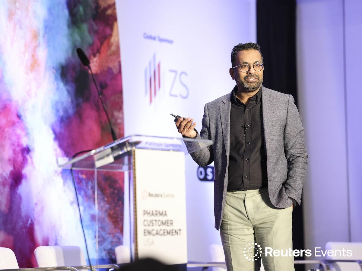 Person on stage at a Reuters Events conference giving a presentation to a room full of people. 