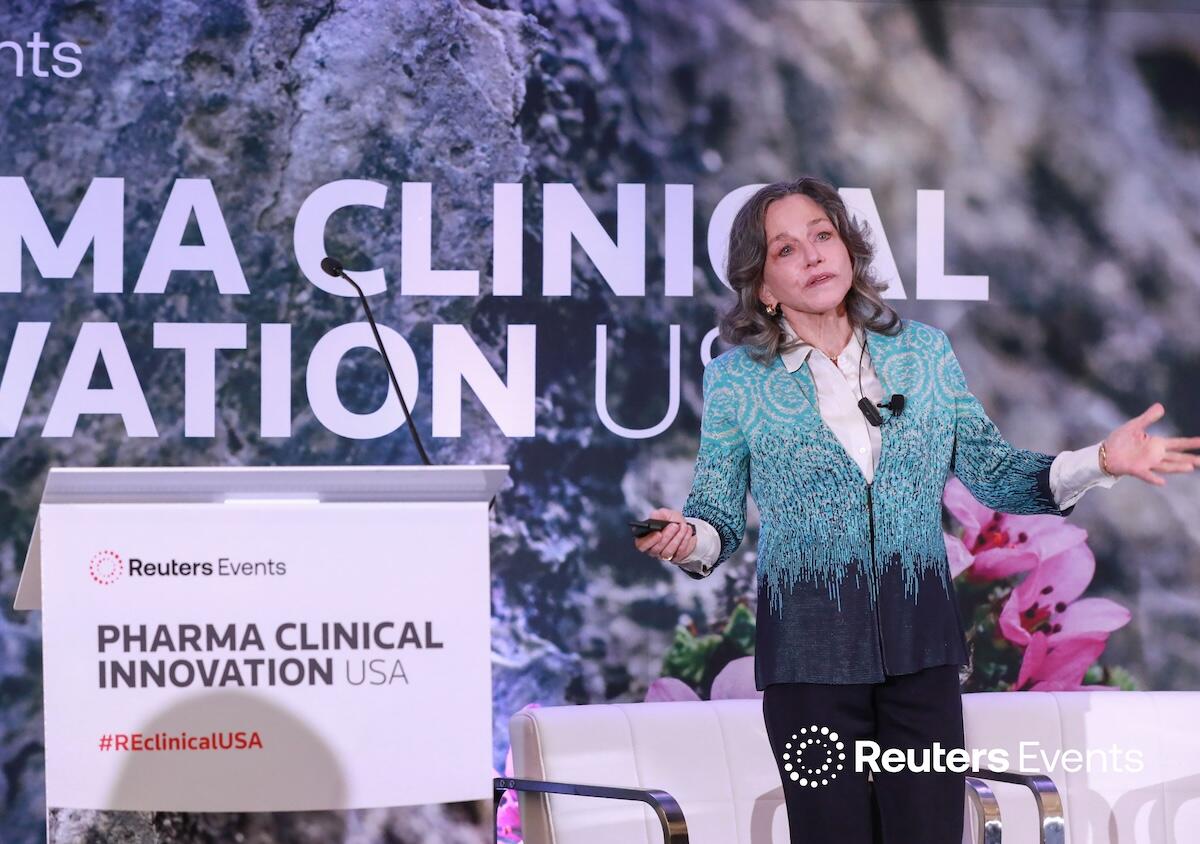 Person on stage at a Reuters Events conference giving a presentation to a room full of people. 