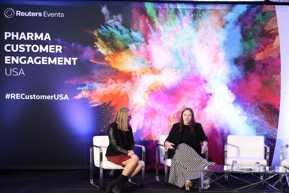 Person on stage at a Reuters Events conference giving a presentation to a room full of people. 