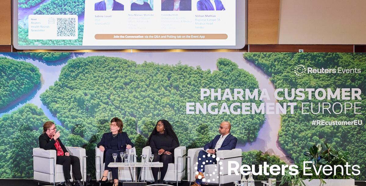 Person on stage at a Reuters Events conference giving a presentation to a room full of people. 