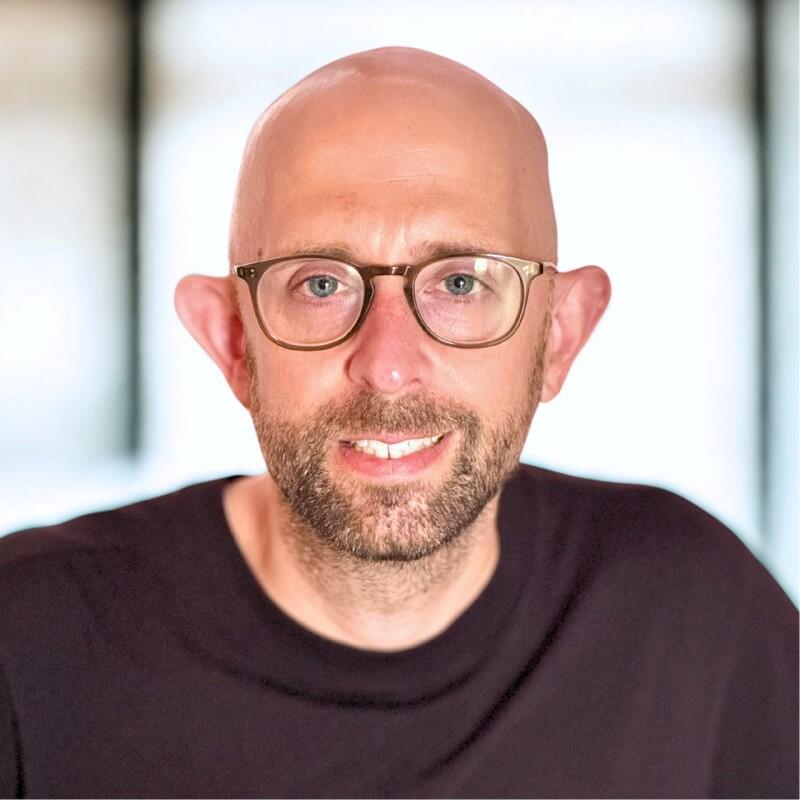 Headshot of Jan Sassmannshausen, a bald man wearing glasses and a black shirt.