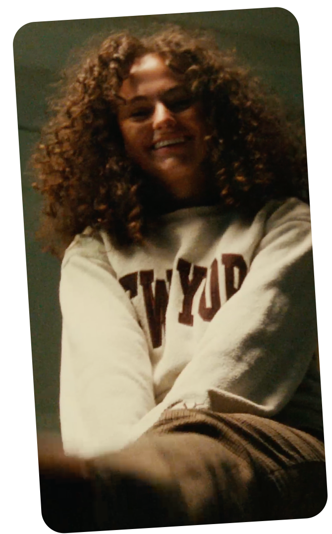 Two young women smiling on a Snapchat video call, with one person shown in a smaller picture-in-picture window at the top and the other filling the main screen below, both with curly hair and bright expressions.