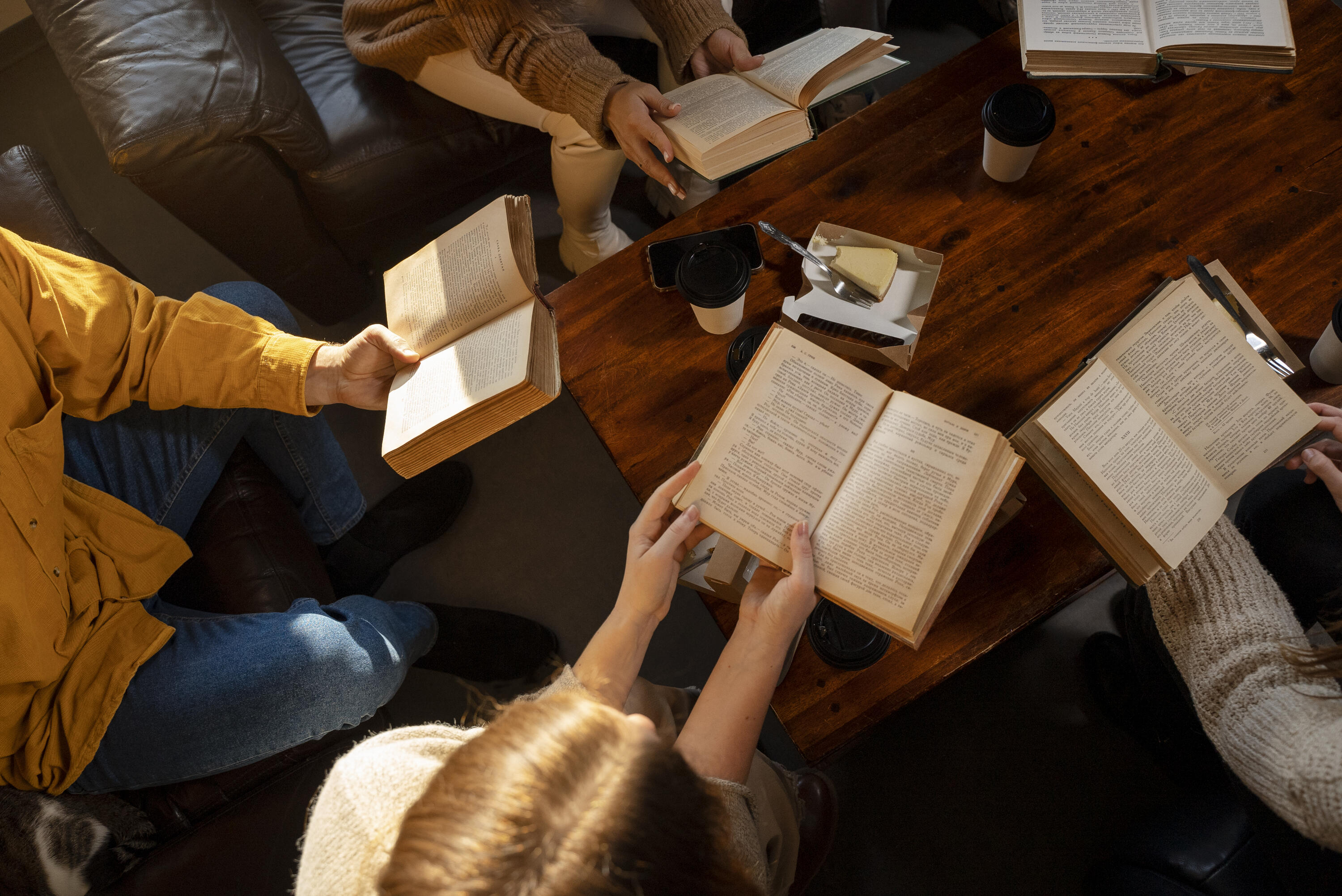 A group of students circled around a library table with open books in their hands. 